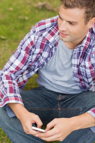 Knappe inhoud student zittend op gras texting — Stockfoto