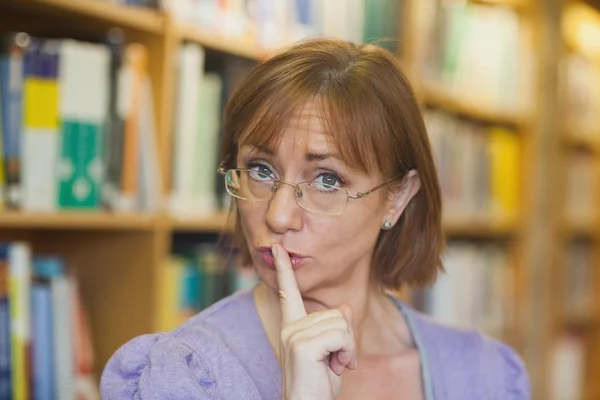 Female librarian giving a sign to be quiet standing in library — Stock Photo, Image