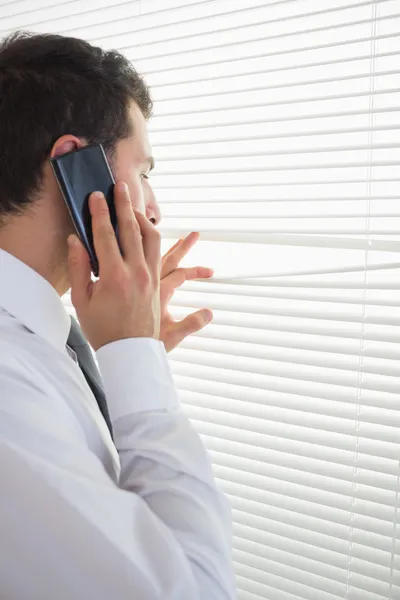 Attraktiver Geschäftsmann spioniert beim Telefonieren durch Rollo — Stockfoto