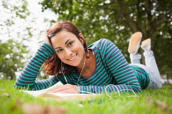 Glada casual student liggande på gräs läser en bok — Stockfoto