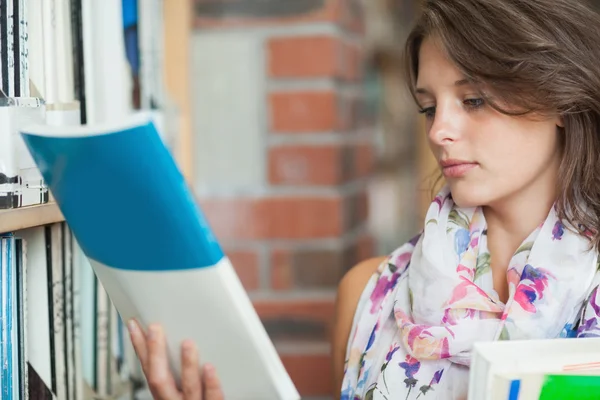 Estudante com livros na prateleira da biblioteca — Fotografia de Stock