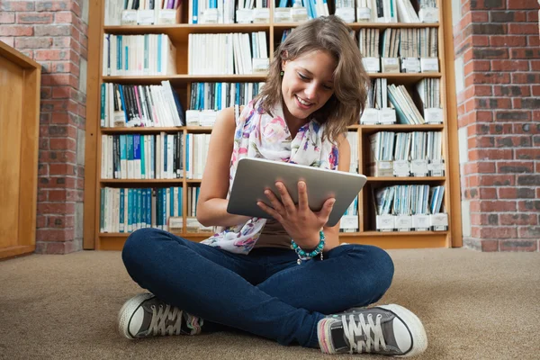 Studentka proti bookshelf pomocí počítače tablet pc na knihovně — Stock fotografie