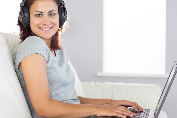 Cheerful casual woman listening to music and using her notebook — Stock Photo, Image