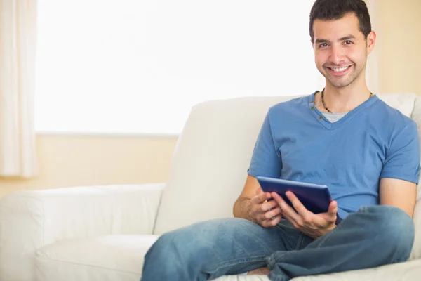 Casual leende man använder tablet sitter på soffan — Stockfoto