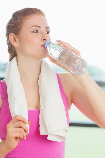 Mujer con toalla alrededor del cuello bebiendo agua en gimnasio — Foto de Stock