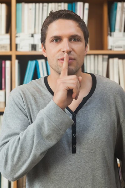 Male librarian making a sign to be quiet in library — Stock Photo, Image