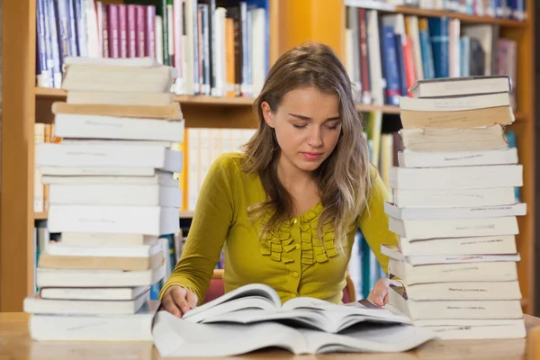 Güzel öğrenci kitap yığınları arasında konsantre — Stok fotoğraf