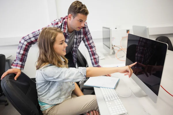 Dos estudiantes sonrientes trabajando en computadora apuntándole — Foto de Stock