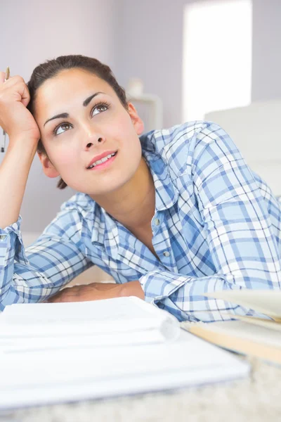 Doordachte brunette student liggend op de vloer in de levende roo — Stockfoto