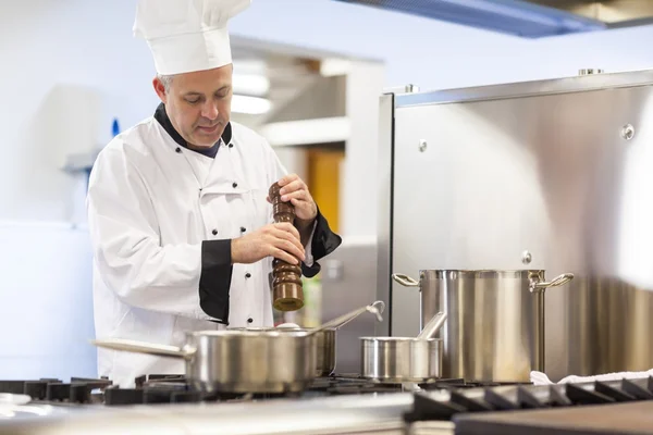 Focused head chef flavoring food with pepper — Stock Photo, Image