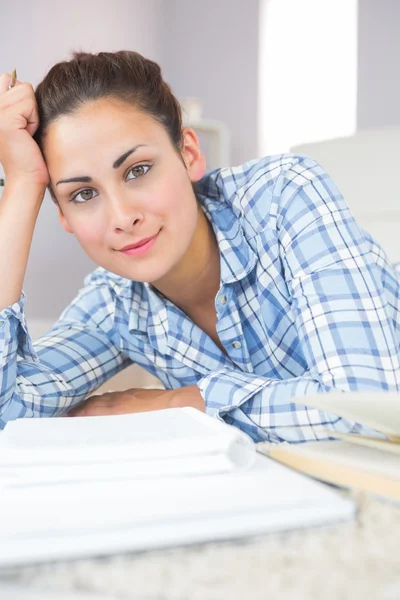 Porträt einer ruhigen jungen Studentin, die Hausaufgaben macht, während sie auf dem Boden liegt — Stockfoto