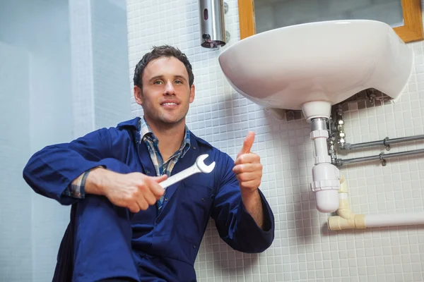 Handsome plumber sitting next to sink showing thumb up — Stock Photo, Image