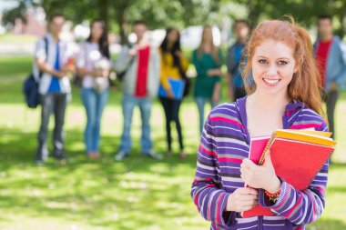 College girl holding books with students in park clipart