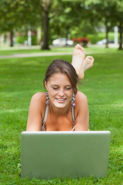 Smiling woman lying on grass and using laptop — Stock Photo, Image