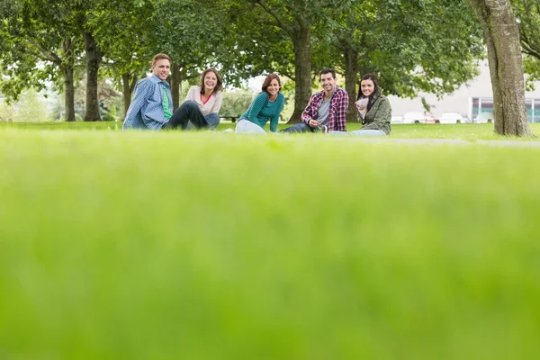 Jovens estudantes universitários sentados na grama no parque — Fotografia de Stock