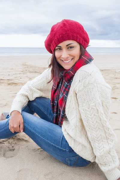 Lachende vrouw in stijlvolle warme kleding zittend op strand — Stockfoto