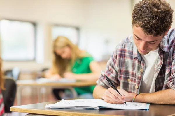 Étudiant avec d'autres écrivant des notes en classe — Photo