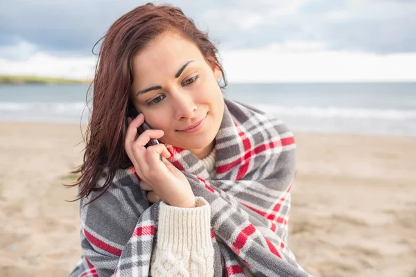 Kvinna täckt med filt med hjälp av mobiltelefon på stranden — Stockfoto