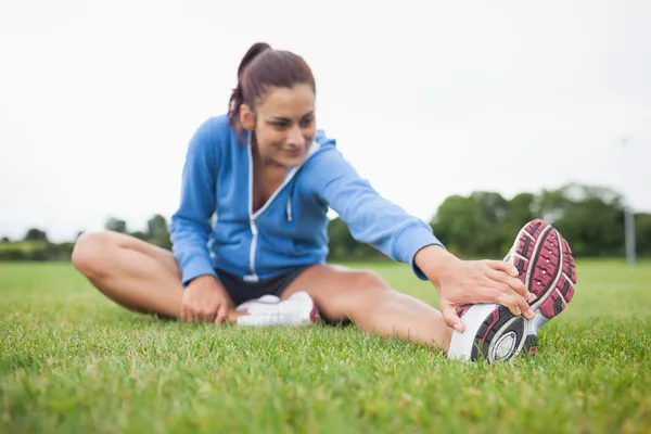 Sportiga kvinnan stretching hennes ben på gräs — Stockfoto