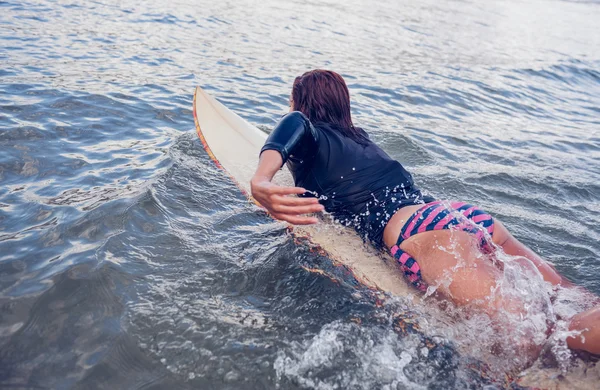 Visão traseira de uma mulher nadando sobre a prancha de surf na água — Fotografia de Stock
