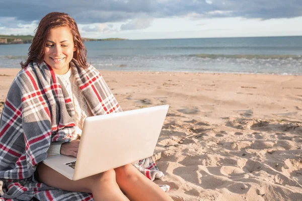 Vrouw bedekt met deken met behulp van laptop op strand — Stockfoto