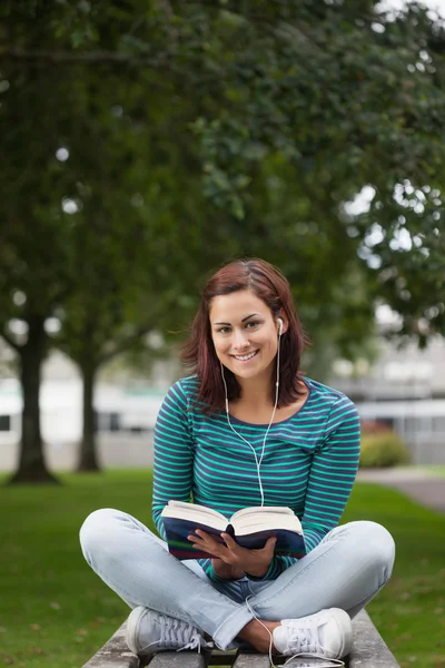 Smiling casual student sitting on bench reading — Stock Photo, Image