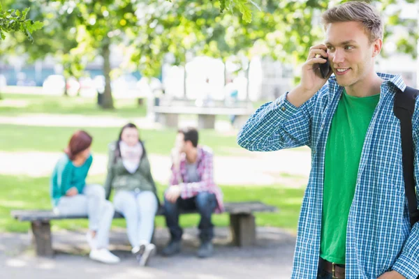 College jongen met behulp van mobiele telefoon met wazig studenten in park — Stockfoto