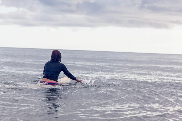 Vista trasera de una mujer con tabla de surf en el agua —  Fotos de Stock