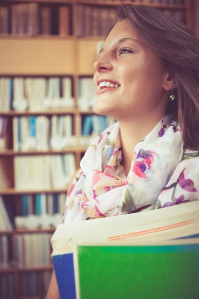 Estudiante sonriente contra estantería en biblioteca — Foto de Stock