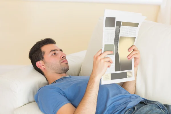 Casual calm man lying on couch reading newspaper — Stock Photo, Image