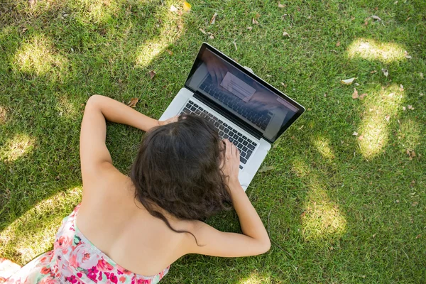 Stijlvolle brunette liggen op het gras met behulp van haar laptop — Stockfoto