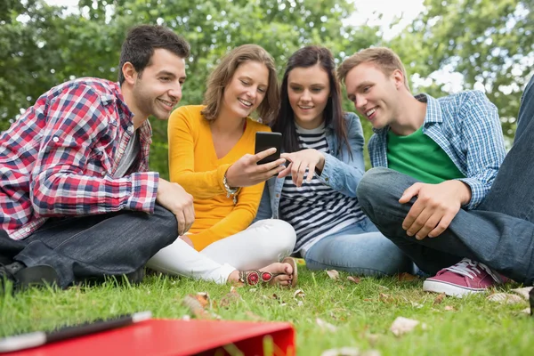 Happy college students looking at mobile phone in park — Stock Photo, Image