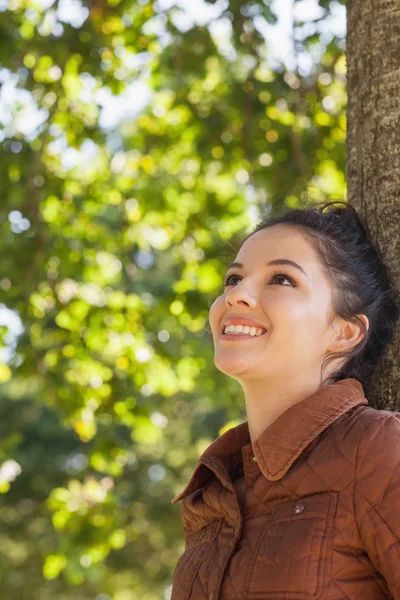 Side view of cheerful young woman leaning against a tree — Stock Photo, Image