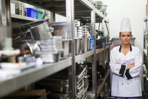 Joven chef frunciendo el ceño de pie brazos cruzados entre estantes —  Fotos de Stock