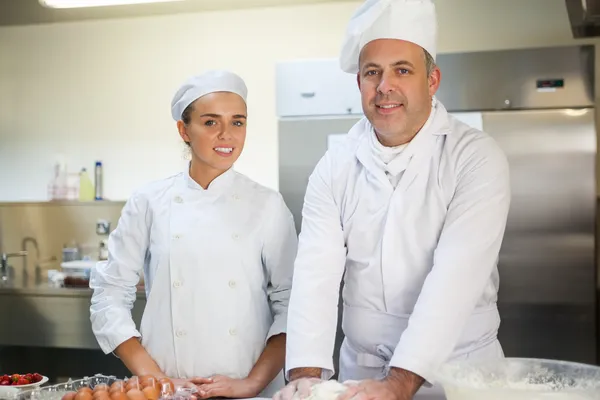 Lächelnder Küchenchef zeigt Auszubildenden, wie man Teig zubereitet — Stockfoto