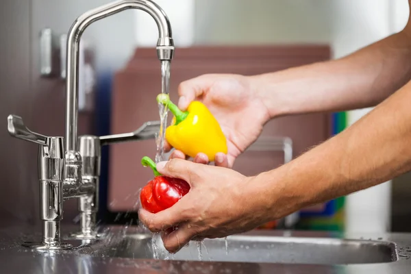 Kitchen porter washing pepper under running tap — Stock Photo, Image