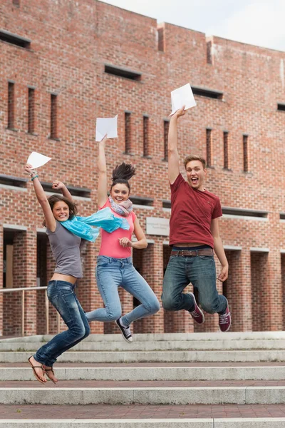Happy students jumping in the air holding exam — Stock Photo, Image