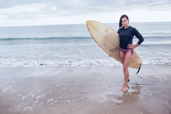 Lunghezza completa di una donna con tavola da surf in spiaggia — Foto Stock