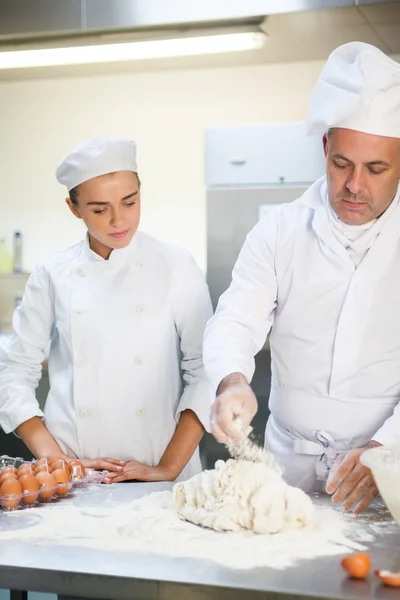 Jefe de cocina serio mostrando aprendiz cómo preparar la masa —  Fotos de Stock