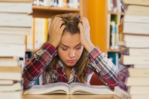 Irriterad söt student som studerar mellan högar av böcker — Stockfoto