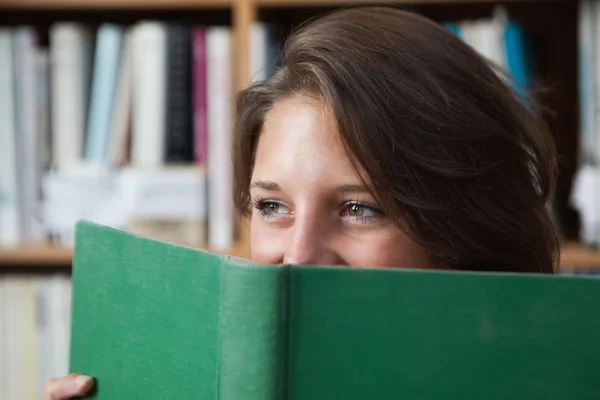 Kitaplığındaki kitap yüzünün önünde tutan kız öğrenci — Stok fotoğraf