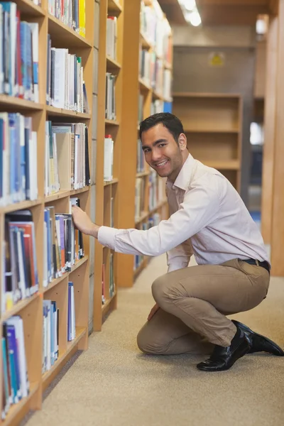 Junger attraktiver Mann kauert vor Bücherregalen — Stockfoto