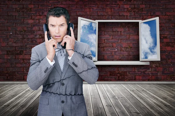 Serious businessman wrapped in cables phoning — Stock Photo, Image