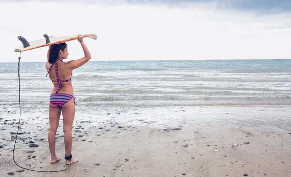 Bikini mujer llevando tabla de surf en la cabeza en la playa —  Fotos de Stock