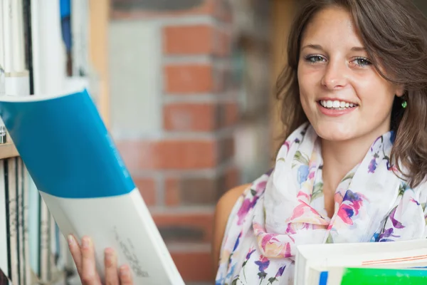 Vrouwelijke student met boeken door de plank in bibliotheek — Stockfoto