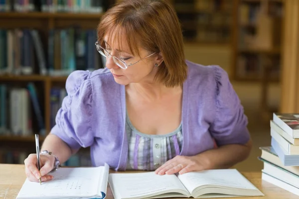 Volwassen vrouwelijke student schrijven van notities op Bureau in de bibliotheek — Stockfoto