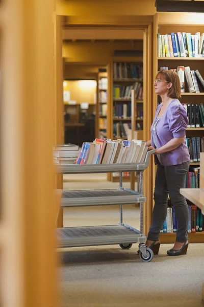 Ernstige vrouwelijke bibliothecaris een kar duwen — Stockfoto