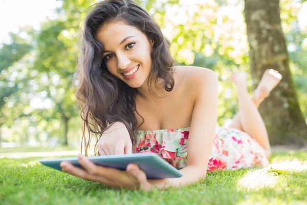 Stylový usměvavá brunetka ležící na trávníku pomocí tabletu — Stock fotografie
