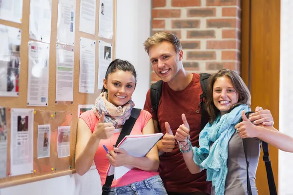 Three smiling students standing next to notice board showing thu — Stock Photo, Image