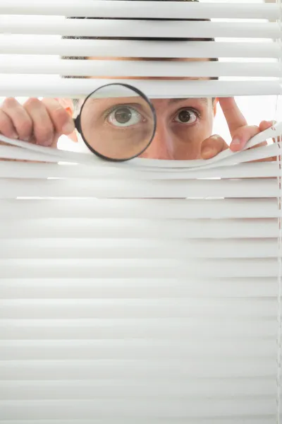 Male eyes spying through roller blind with magnifier — Stock Photo, Image